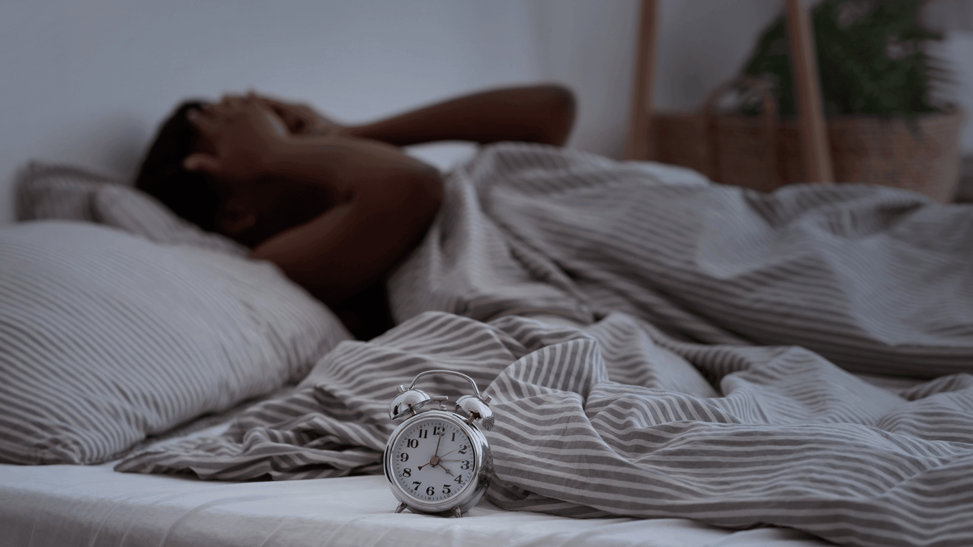 Person lying in bed with an alarm clock nearby, illustrating the struggle with sleep disorders and insomnia